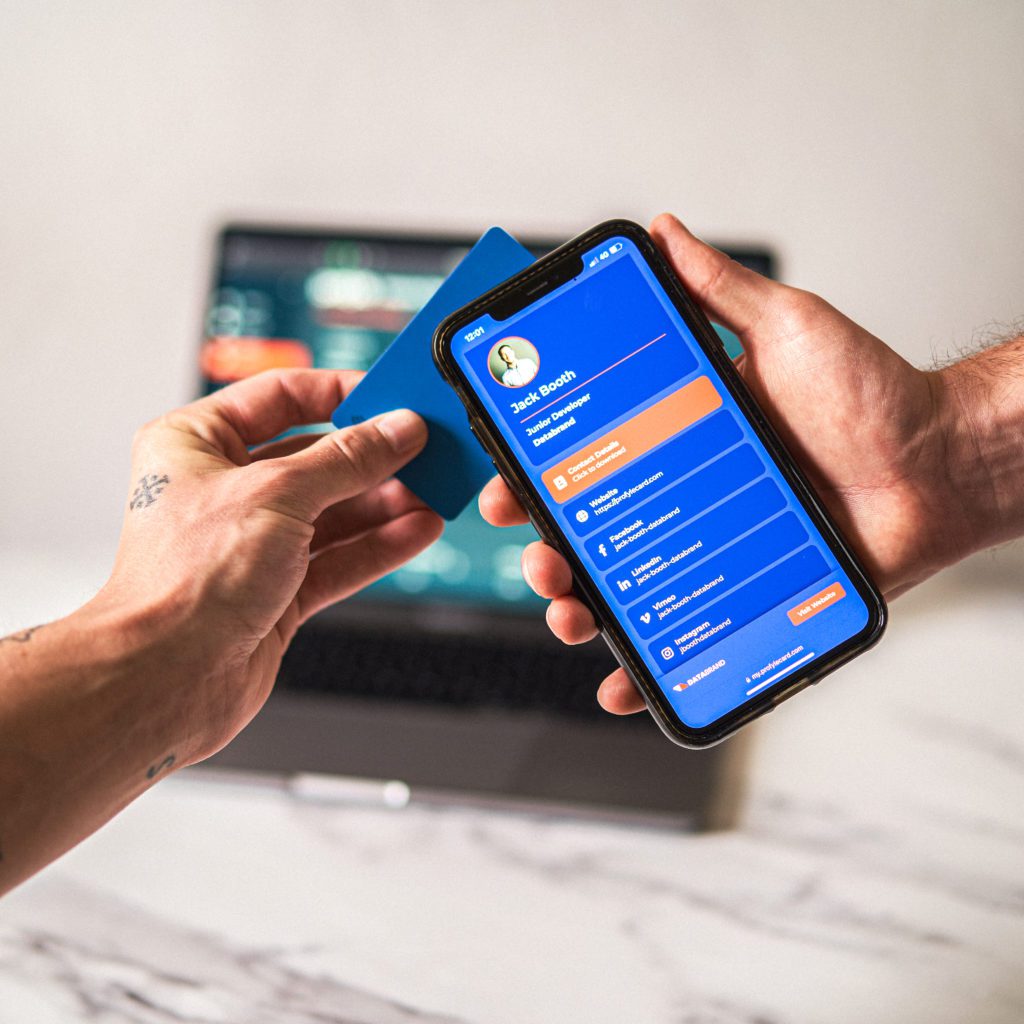 Hand holding blue card tapping a smartphone displaying a digital business card for Jack Booth, Junior Developer.