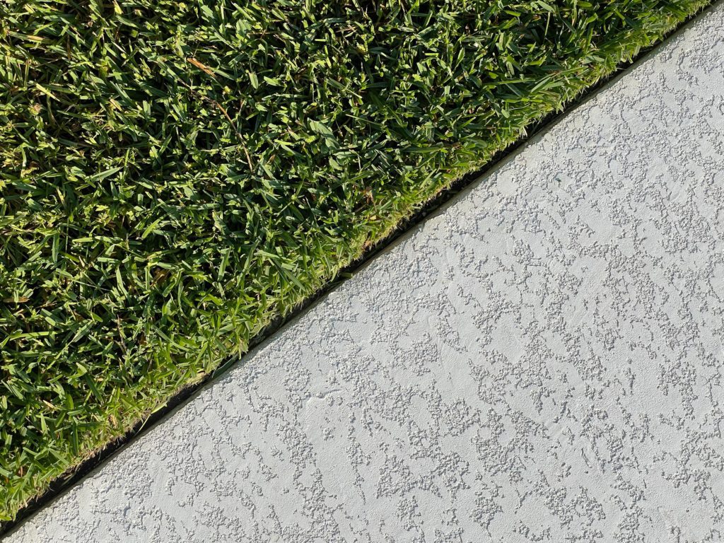 Diagonal view of green grass next to a textured light grey concrete surface.