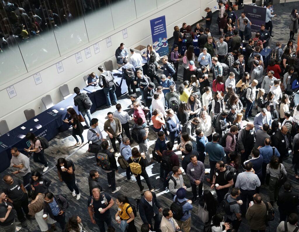 Overhead view of a large crowd at an indoor event with 'Product School' and 'Mixpanel' banners.