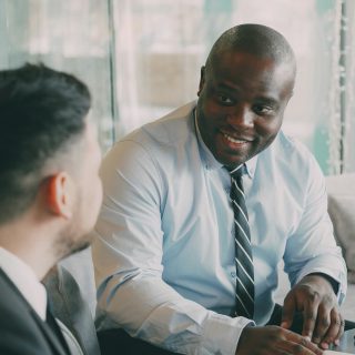 Two men in business attire talking, one smiling warmly at the other.