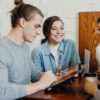 Two people, a man and a smiling woman, looking at a tablet on a wooden table.