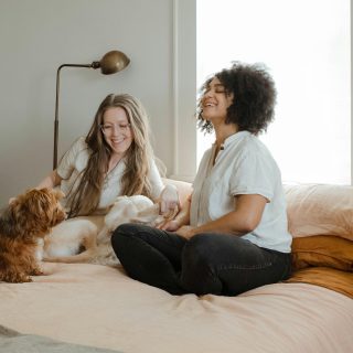 Two smiling women on a bed with two small dogs.