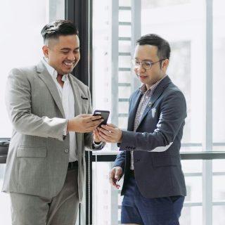 Two smiling men in suits look at a smartphone, one pointing at the screen.